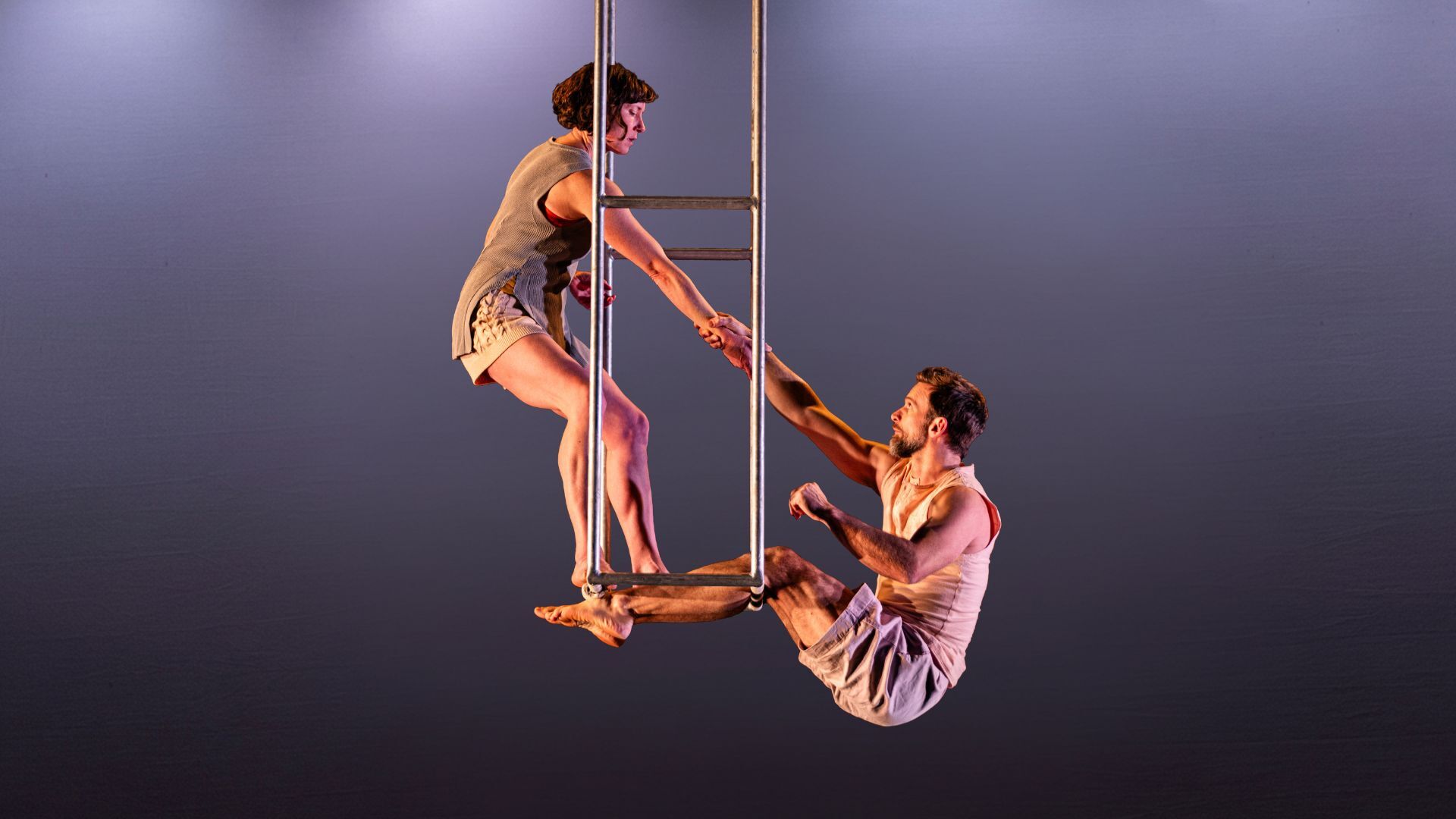 Charlotte Mooney and Alex Harvey reaching for each other's hands from a suspended metal ladder.