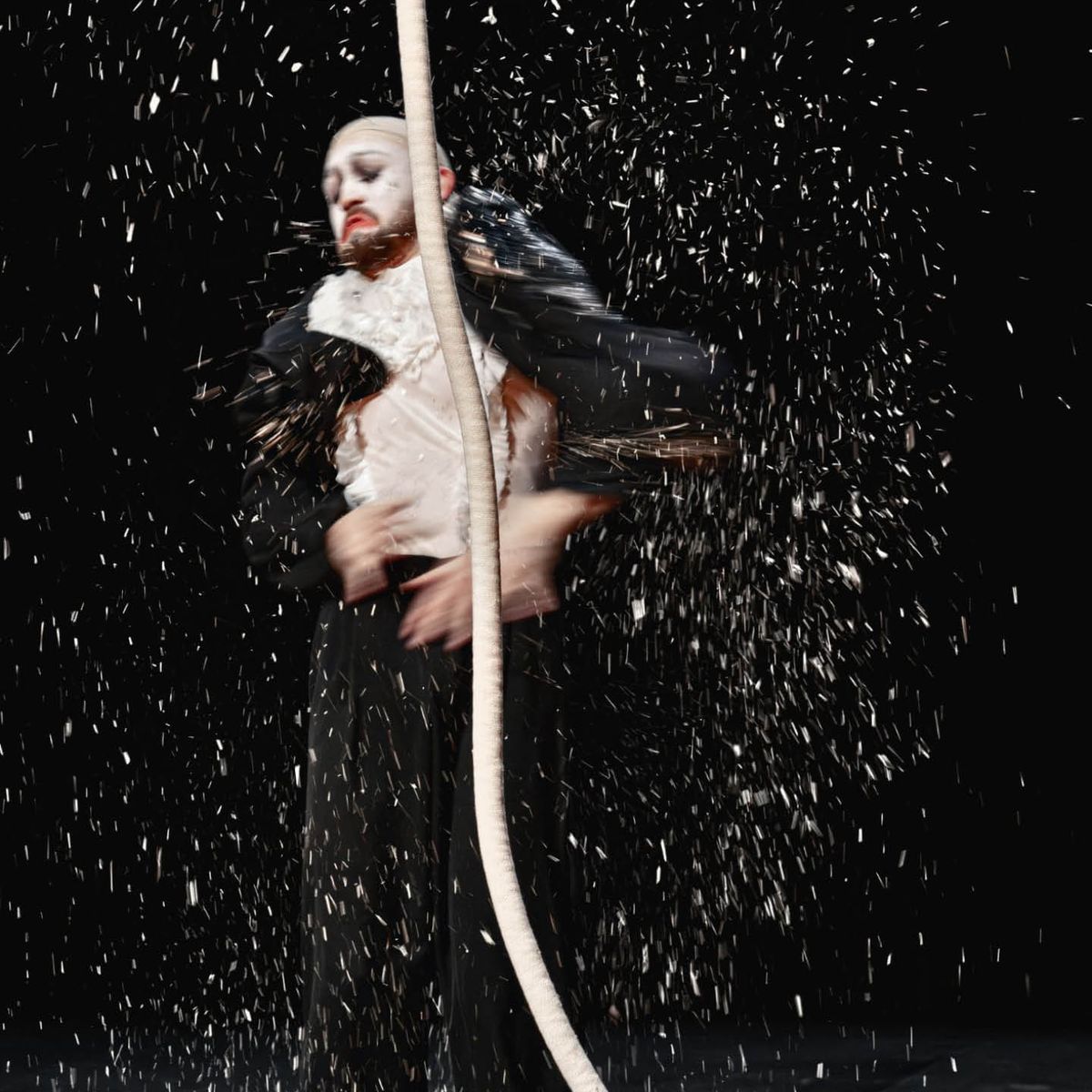Aurora Dini hanging by one hand from an aerial hoop against a black background