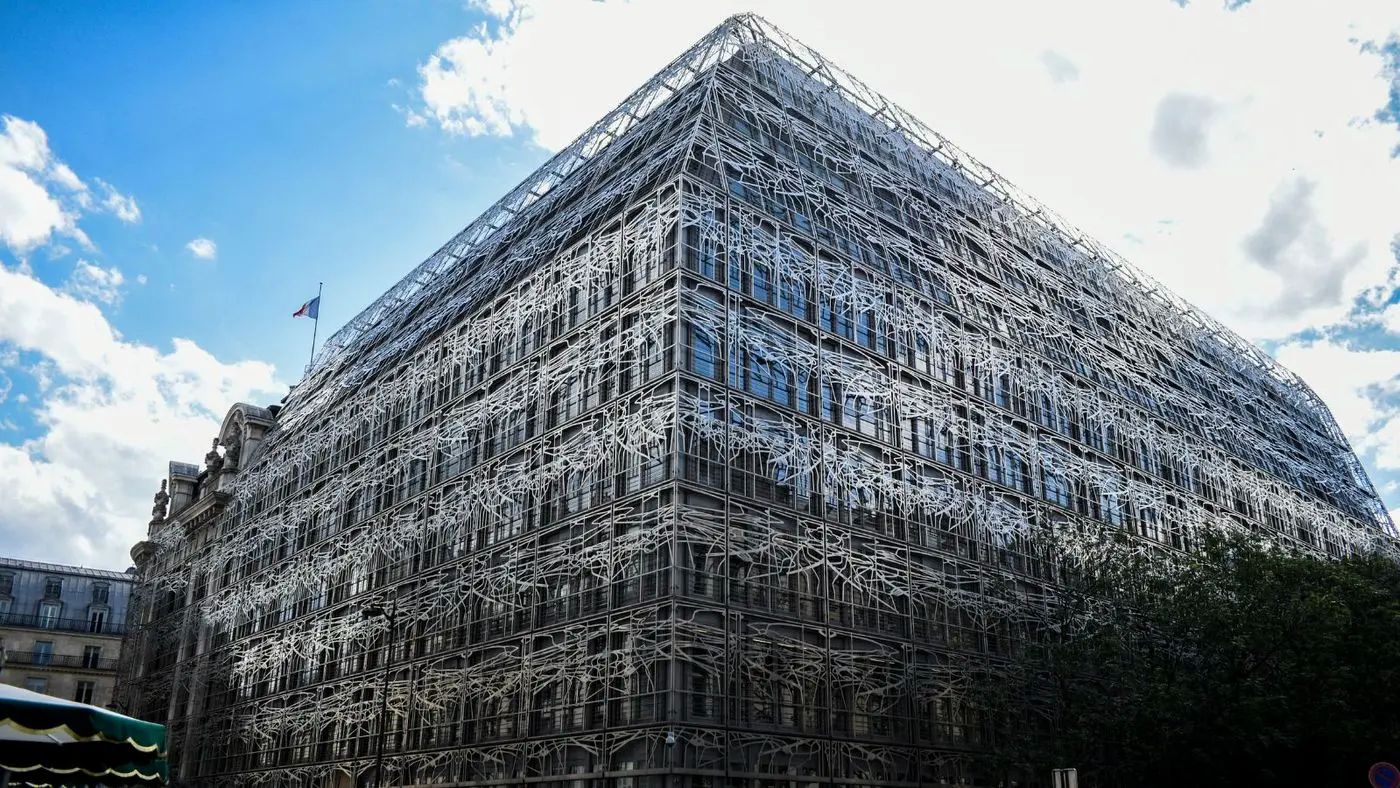 The corner of the French Ministry of Culture building in Paris, its glass facade wrapped in a white metal lattice, the tricolore flying from the roofline against a blue sky