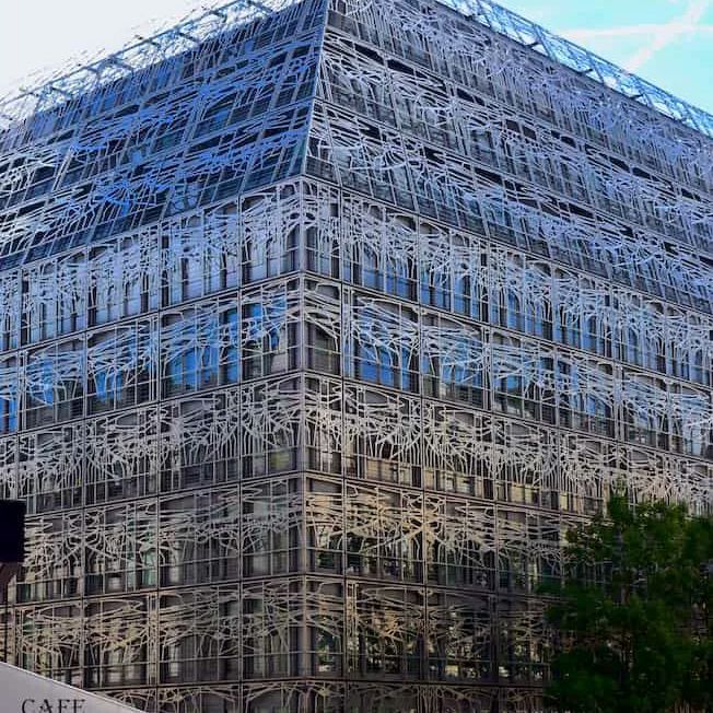 The corner of the French Ministry of Culture building in Paris, its glass facade wrapped in a white metal lattice, the tricolore flying from the roofline against a blue sky