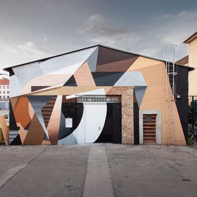The Katapult building in Berlin Oberschöneweide, its brick facade painted with a large geometric mural in pale blue, peach and black, with white double doors at the centre