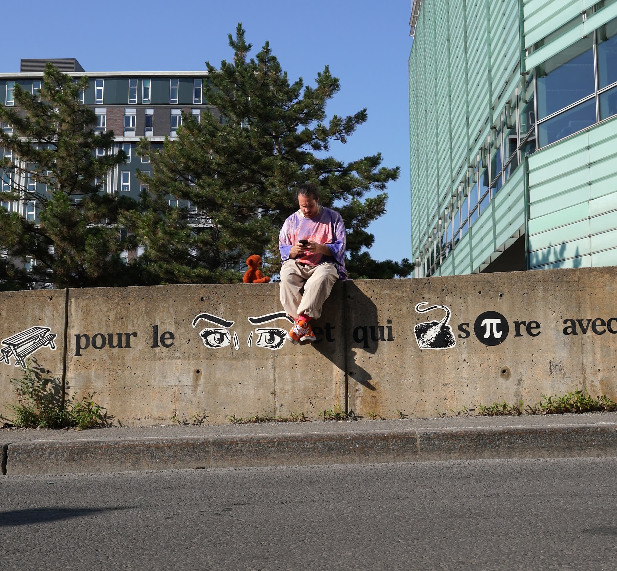 Vincent sitting on a concrete wall outside the Grande Bibliothèque in Montreal, reading his phone